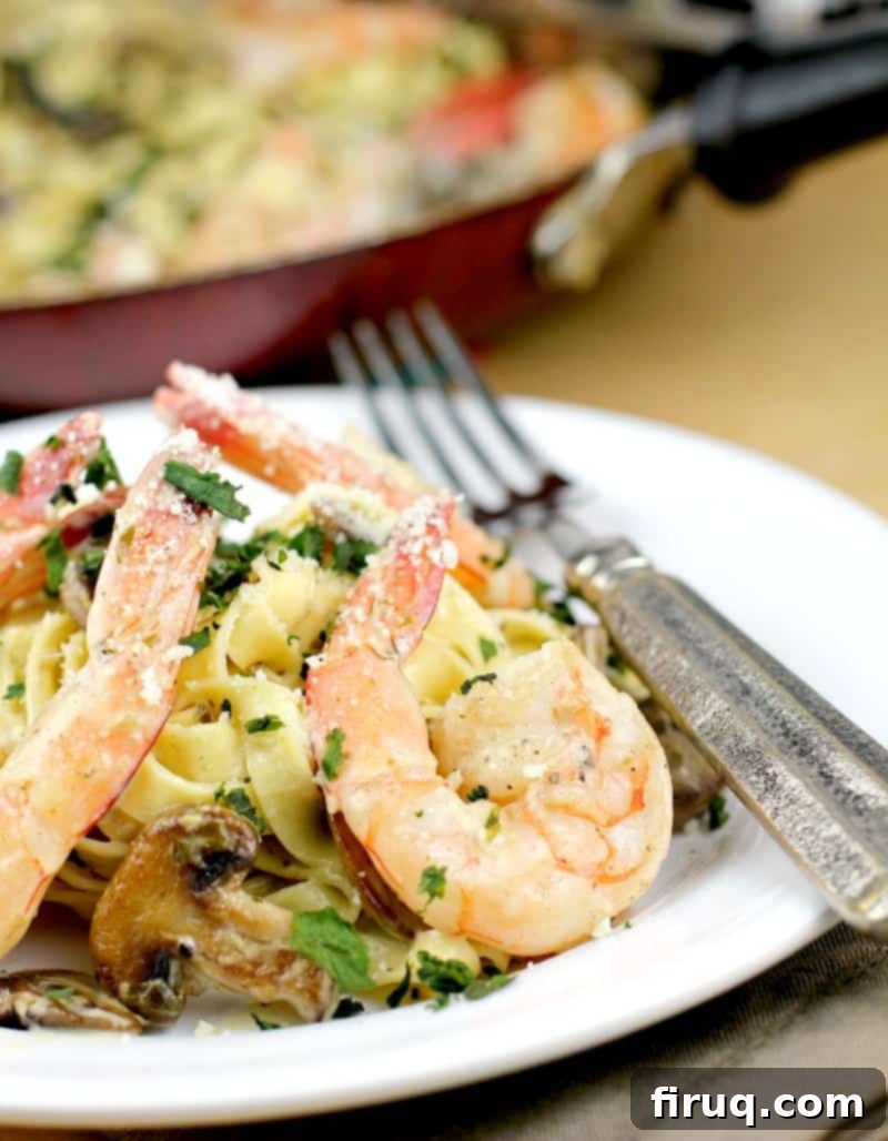 Luscious Creamy Pesto Shrimp Pasta 2 A beautifully plated creamy pesto pasta with shrimp on a white dish, with a fork in the foreground and a skillet containing the remaining pasta in the background, highlighting its romantic dinner appeal.