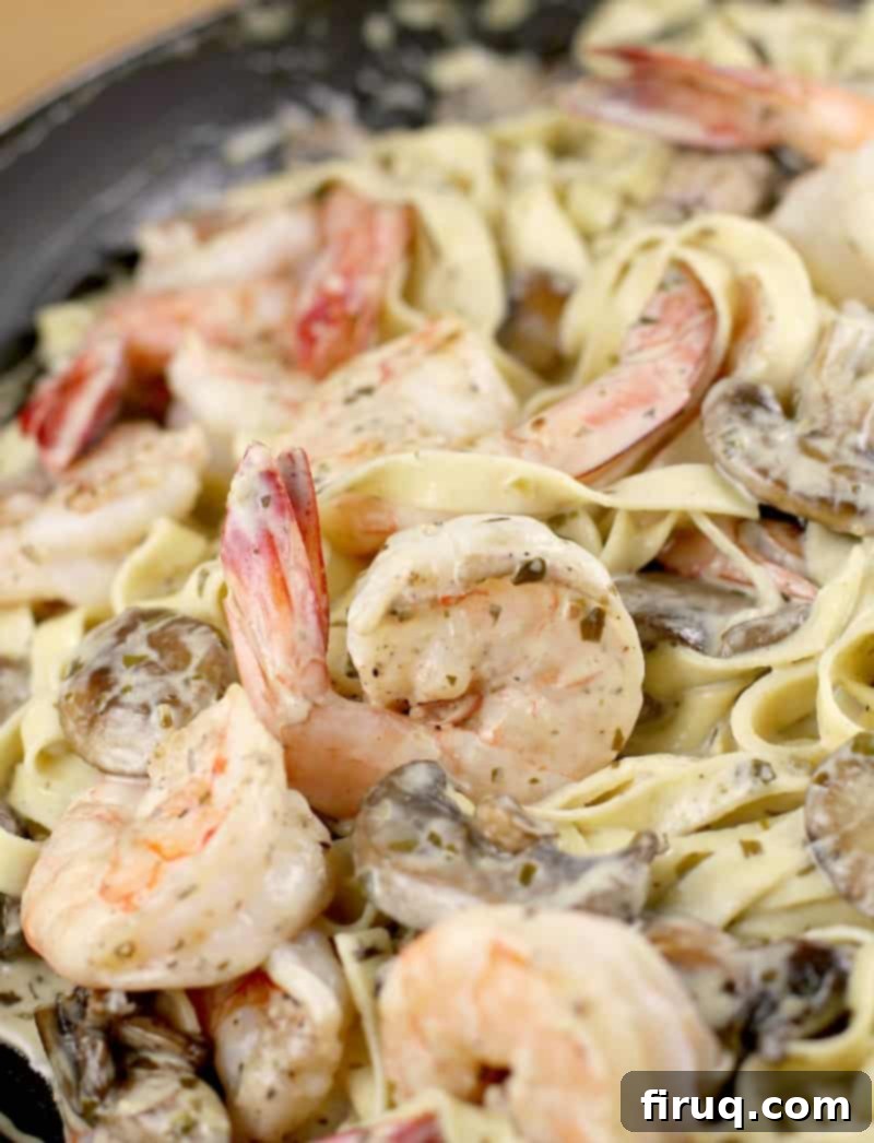 Luscious Creamy Pesto Shrimp Pasta 6 A close-up view of shrimp and mushrooms being mixed into the creamy pesto sauce with pasta in a skillet, showing the rich coating and vibrant colors.