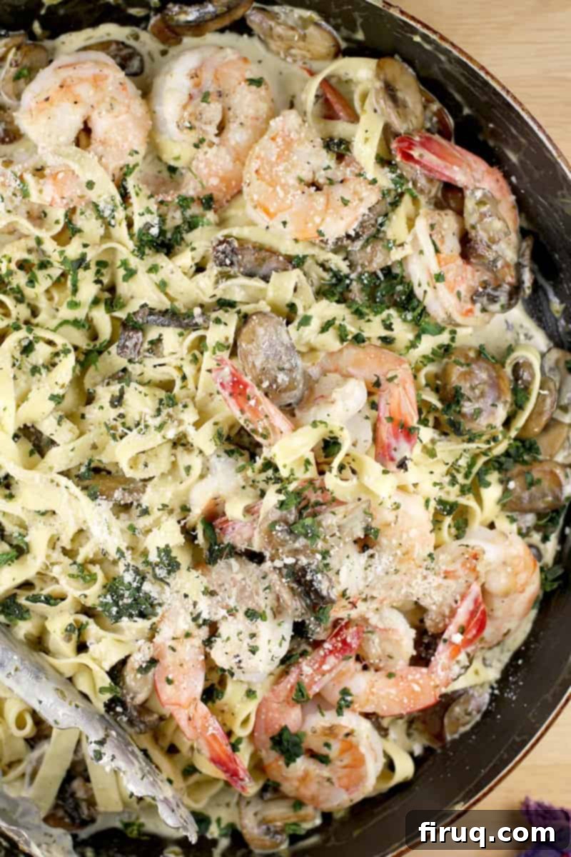 Luscious Creamy Pesto Shrimp Pasta 8 A top-down view of creamy pesto pasta with shrimp garnished with fresh basil and Parmesan cheese, served in a skillet with tongs in the corner, highlighting its inviting presentation.