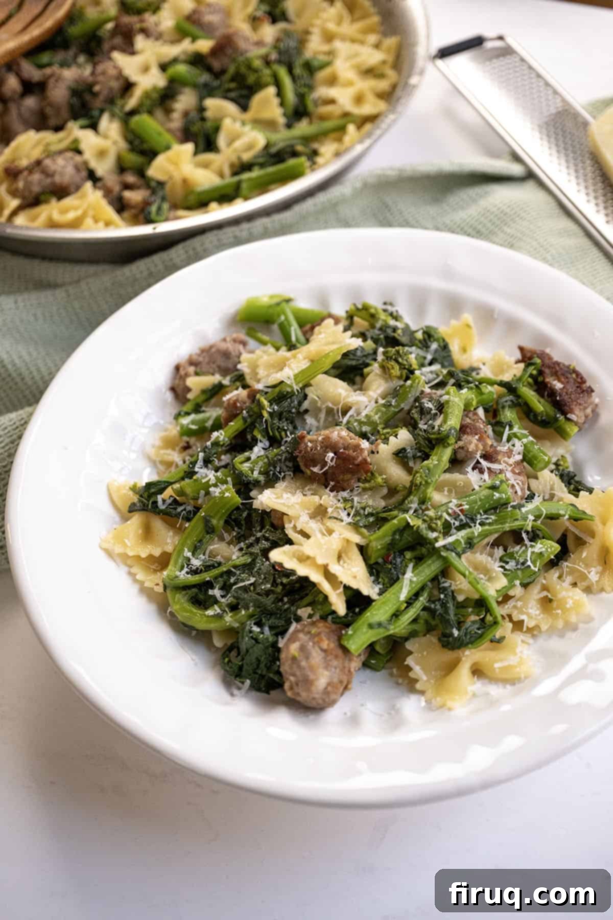 Sausage and Rapini Pasta 2 Farfalle with sausage and broccoli rabe, topped with parmesan on a plate.