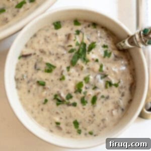 Velvety Mushroom Mascarpone Soup 10 Creamy mushroom soup in a cup with a spoon, garnished with fresh herbs.