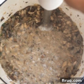 Velvety Mushroom Mascarpone Soup 7 Using an immersion blender to partially blend the creamy mushroom soup, creating a desirable chunky yet smooth texture.