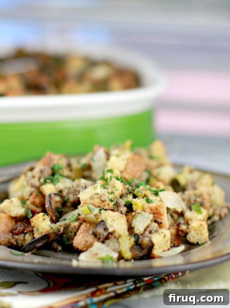 The Ultimate Holiday Stuffing 3 Serving of homemade sausage stuffing plated on a brown ceramic plate, with the full casserole dish in the background