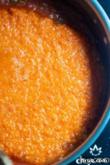 Velvety Red Pepper Sauce 10 Blended red pepper puree being poured into the simmering tomato sauce in a pan, ready for final simmering.