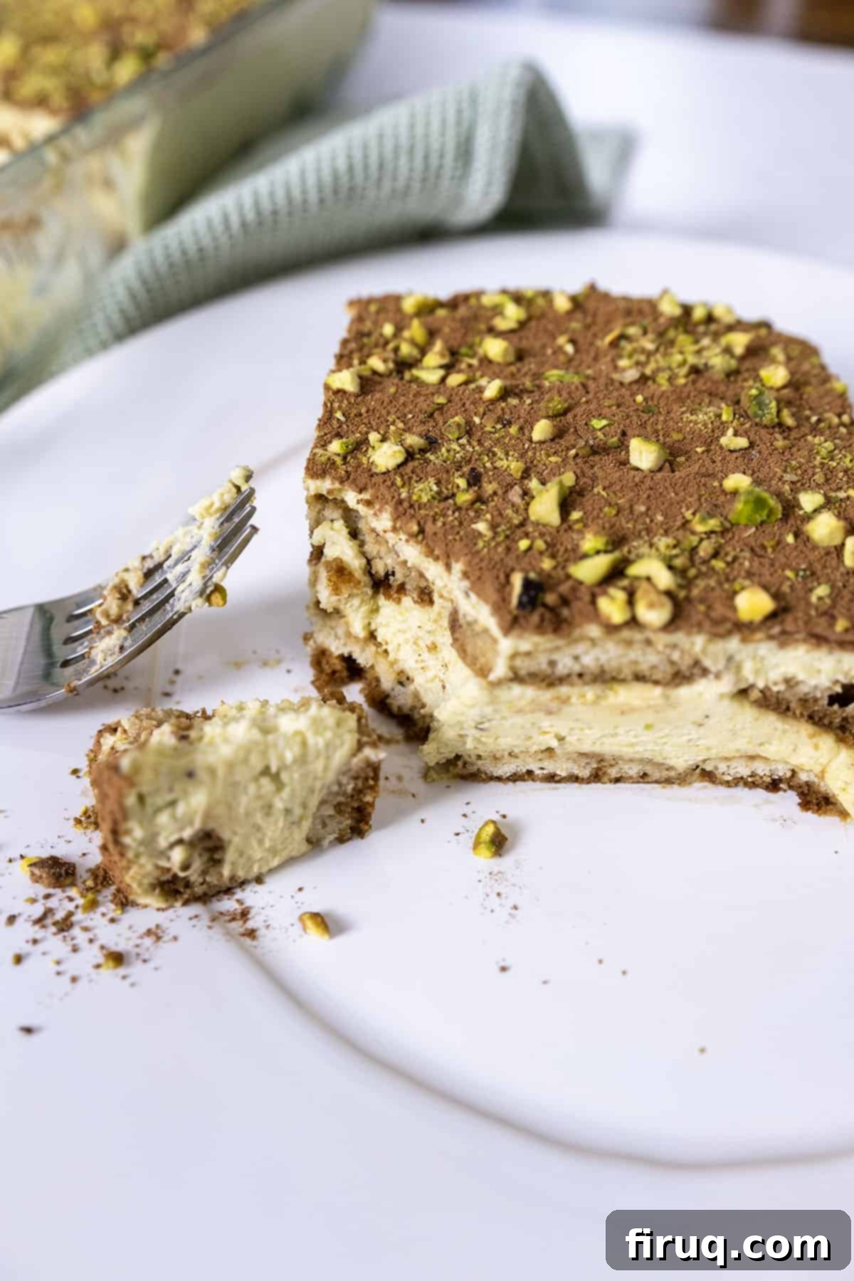 Emerald Dream Tiramisu 2 A slice of Pistachio Cream Tiramisu on a plate with a fork having scooped out a creamy bite.
