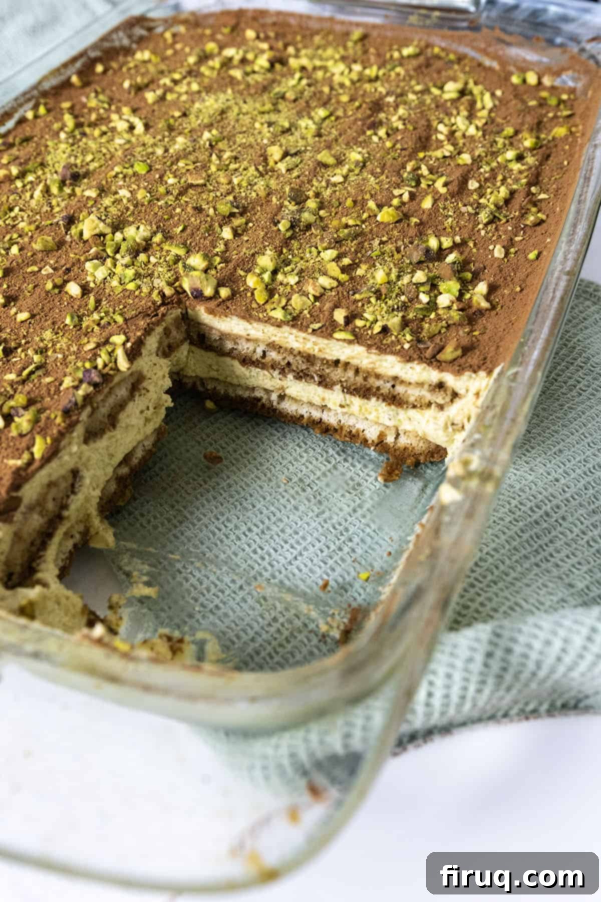 Emerald Dream Tiramisu 15 A large glass baking dish of Pistachio Cream Tiramisu with a square slice removed, revealing the layers.