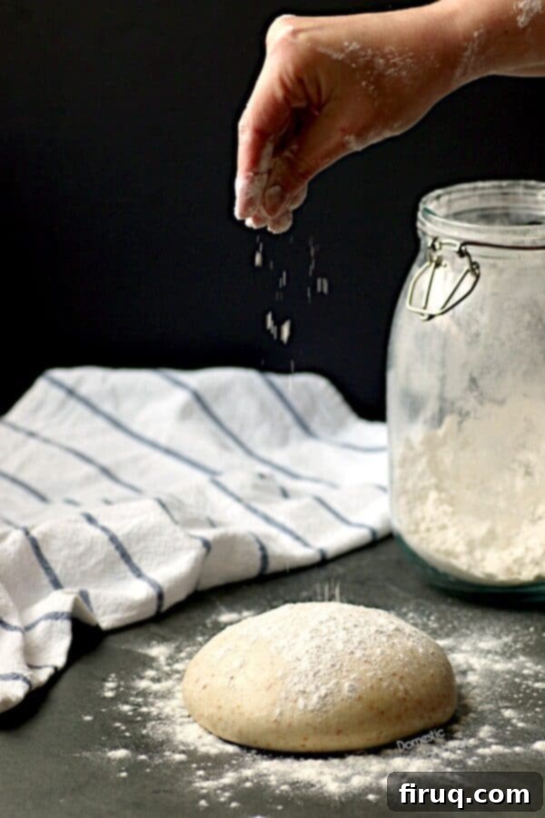 Flouring Pizza Dough A hand gently sprinkling flour over a round of smooth, elastic homemade pizza dough, showcasing its readiness for shaping.