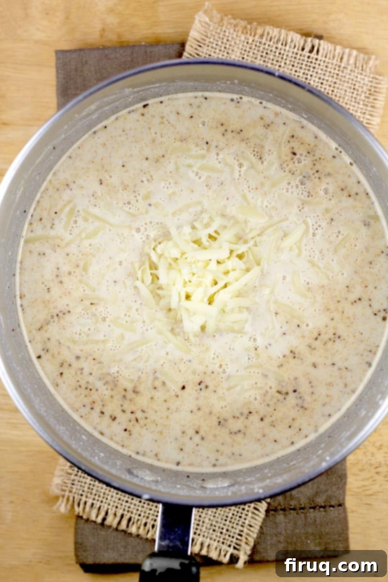 Decadent Crab Mac and Cheese 4 bechamel sauce in a saucepan with shredded cheese added in the center