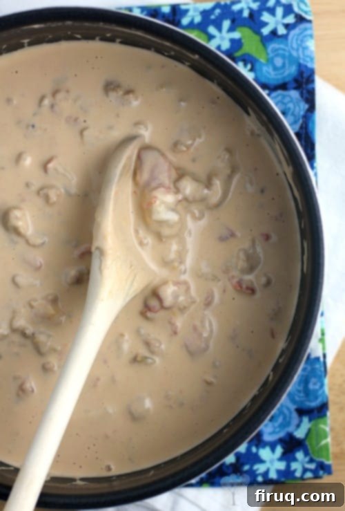Beer-Glazed Kielbasa and Sausage with Stout Queso 5 The finished sausage and Guiness extra stout beer cheese sauce in a saucepan with a wooden spoon; blue floral napkin in the background