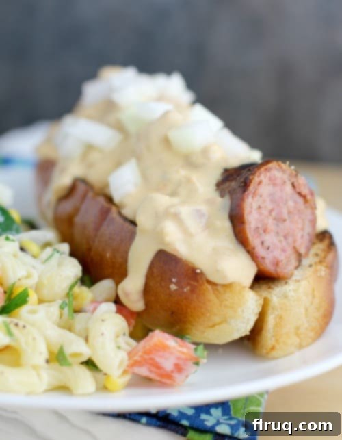Beer-Glazed Kielbasa and Sausage with Stout Queso 9 similar view of a finished beer kielbasa with queso, this time in a hot dog bun, white plate, with potato salad on the side