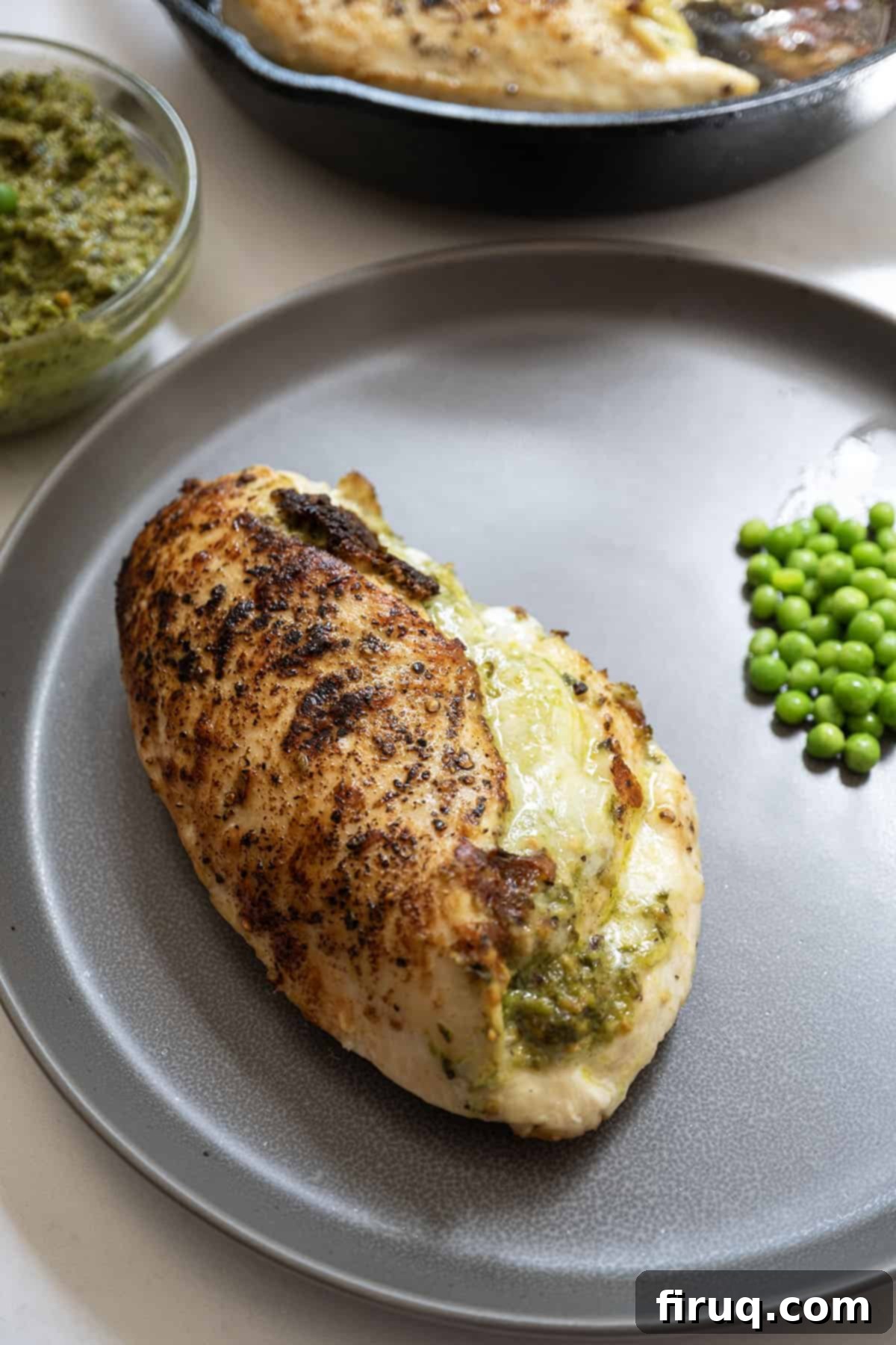 Perfect Pesto Stuffed Chicken 2 Pesto stuffed chicken on a plate with vibrant pea pesto and melted mozzarella, garnished with fresh peas and basil, ready to be served.