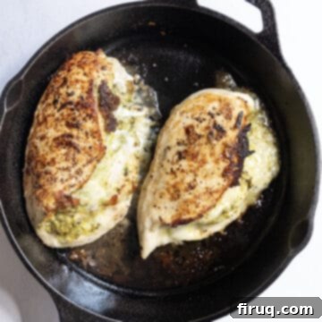 Perfect Pesto Stuffed Chicken 9 Perfectly cooked pesto stuffed chicken breast, with melted cheese oozing out, resting on a cutting board after being removed from the oven.