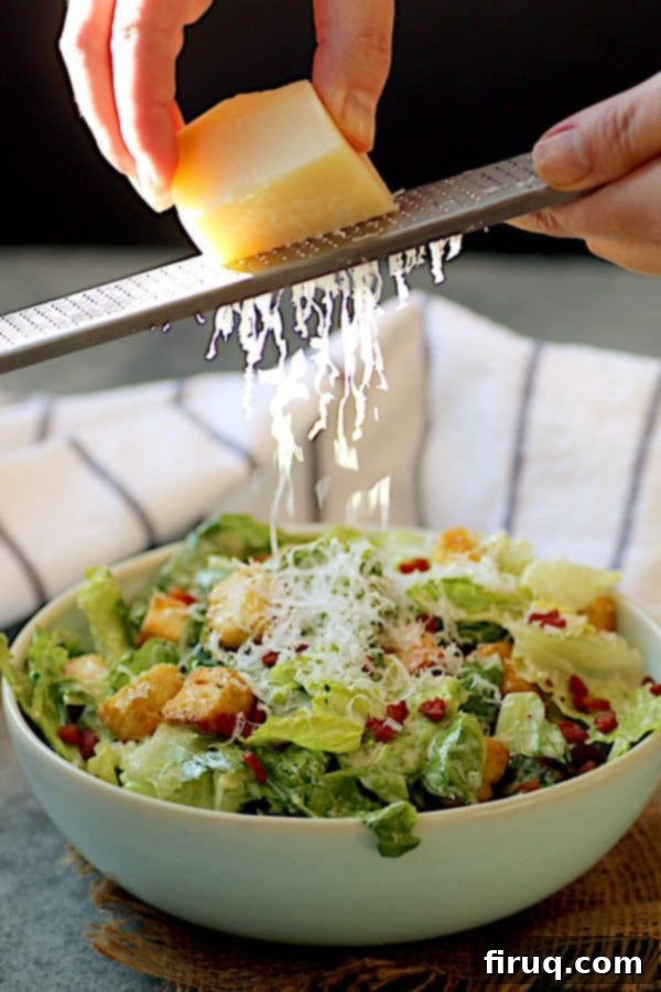 Garnishing Caesar Salad with Parmesan Hands grating fresh Parmesan cheese generously over a prepared Caesar salad.