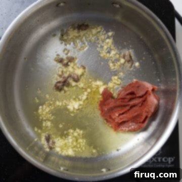 Robust Red Clam Linguine 5 Rich red tomato paste caramelizing at the bottom of a saucepan, stirred with garlic.
