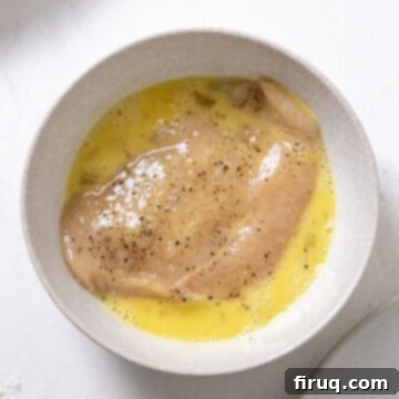 Ultimate Chicken Pizzaiola 4 Seasoned chicken breast being dipped into an egg wash, preparing it for dredging.