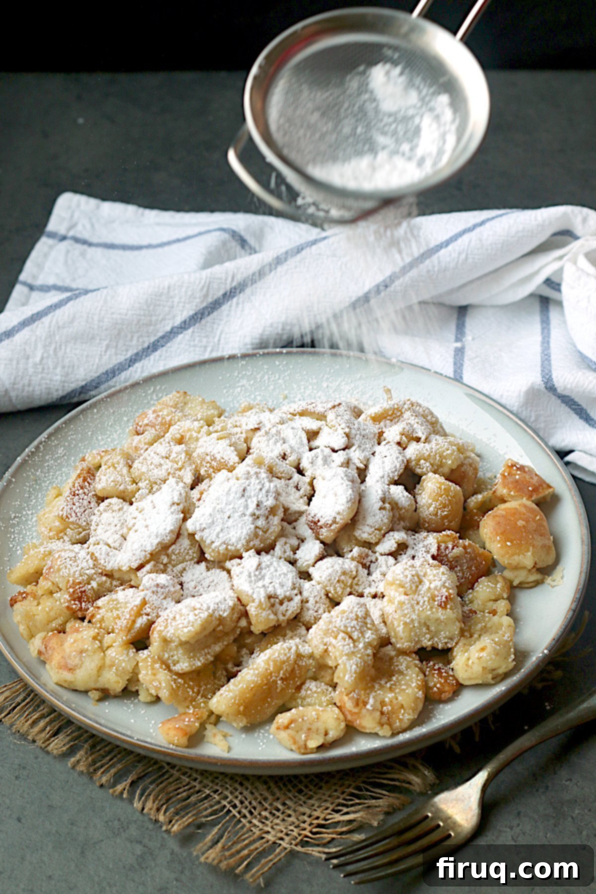 Kaiserschmarrn with Powdered Sugar Austrian Shredded Pancake on a plate with powdered sugar being sifted on top.