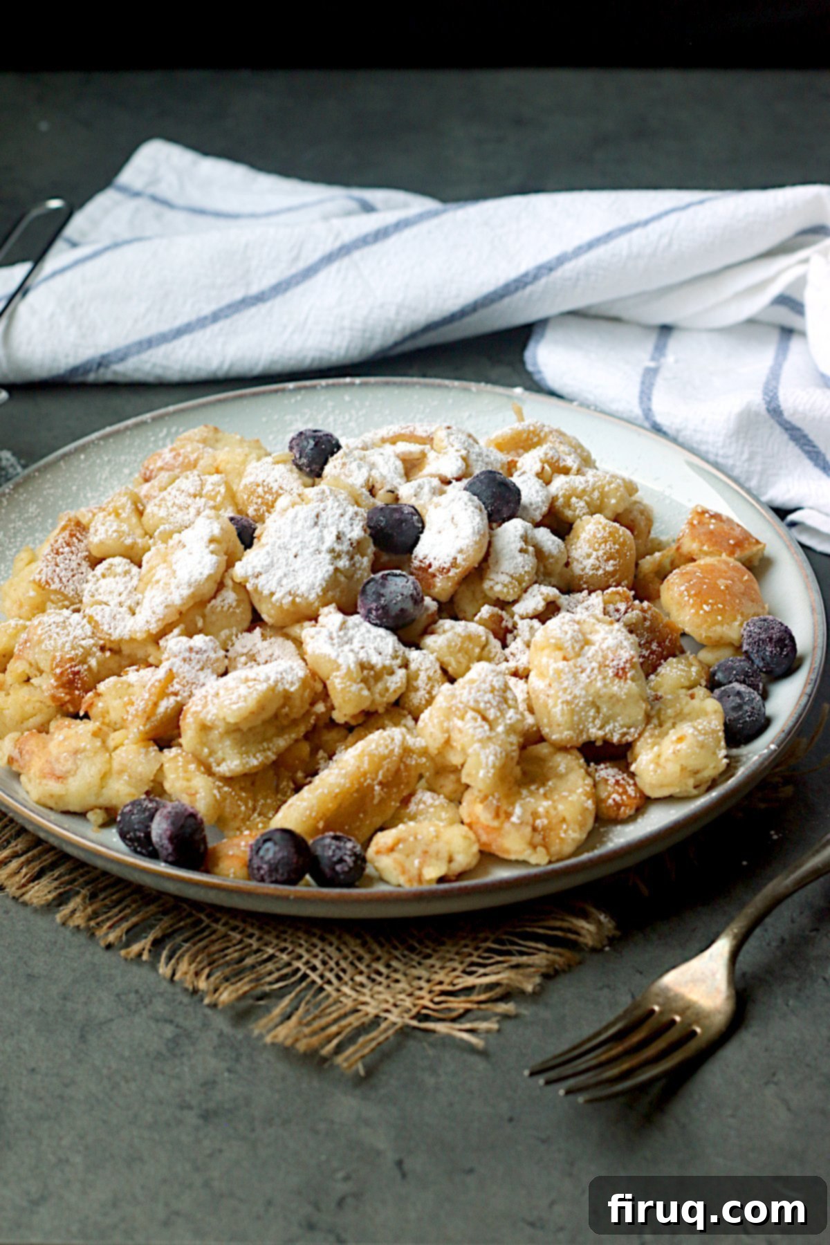 Plated Kaiserschmarrn with Fruit Austrian Shredded Pancake with blueberries and powdered sugar on a plate.
