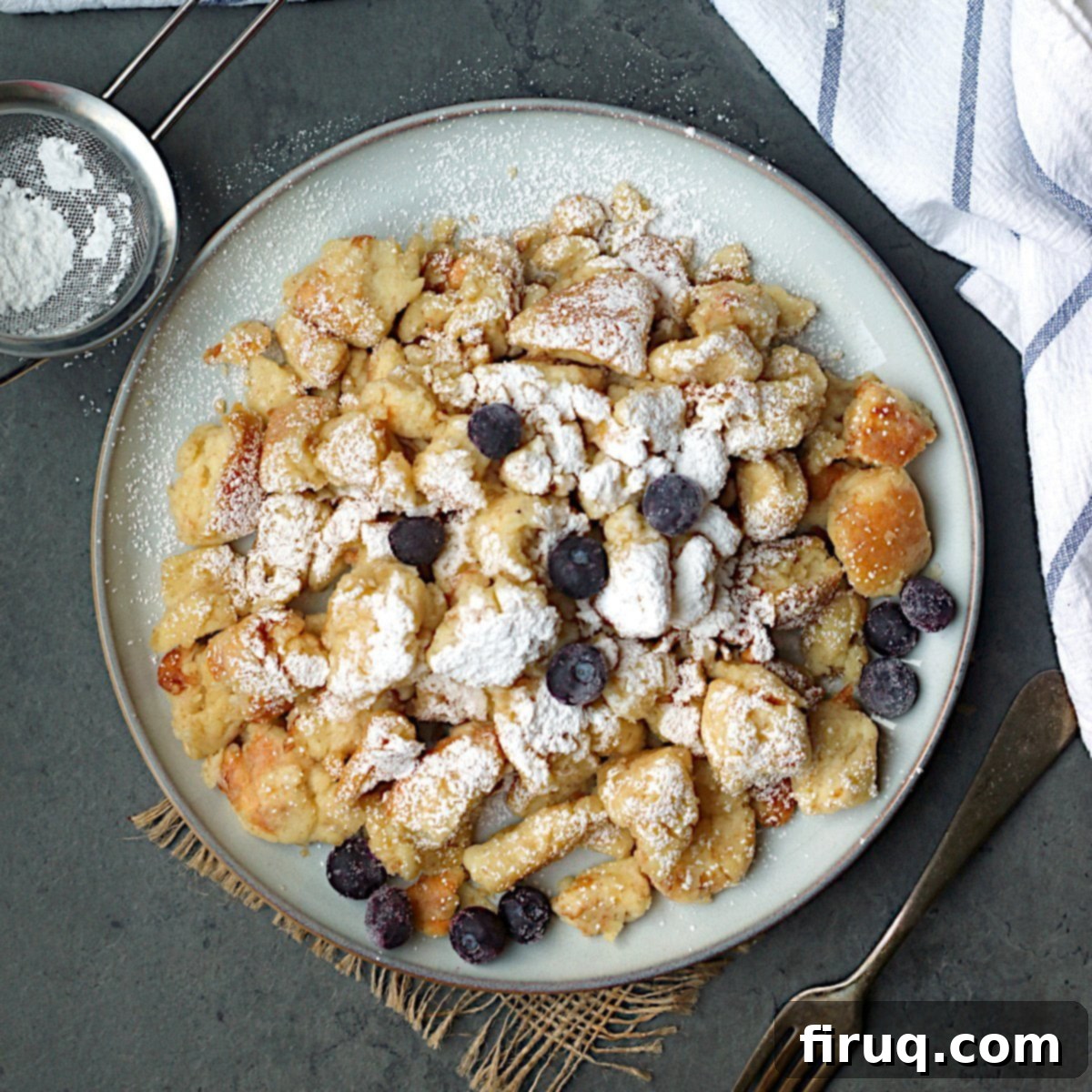 Finished Kaiserschmarrn Ready to Serve Overhead photo of Austrian Shredded Pancake with blueberries and powdered sugar on a plate.