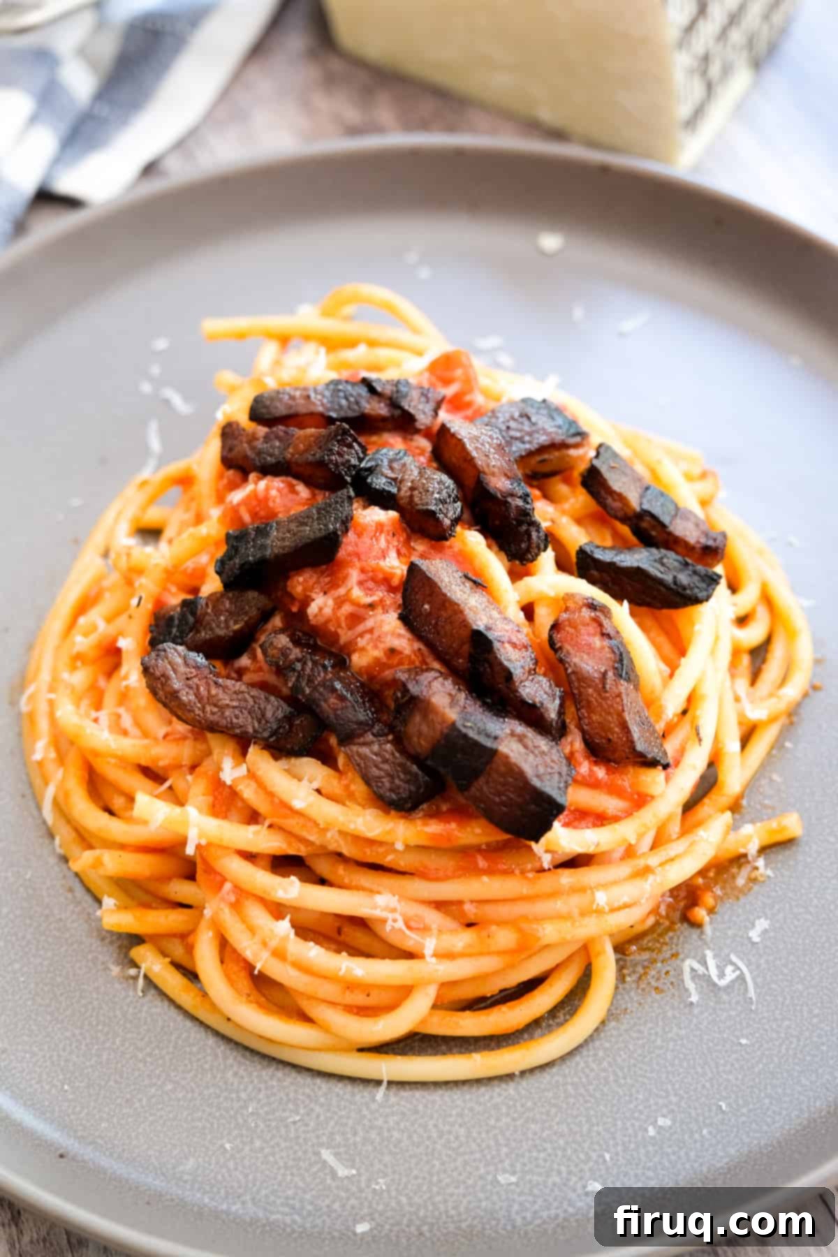 Bucatini Amatriciana 12 A close-up shot of a perfectly plated Bucatini Amatriciana, garnished with more crispy guanciale and freshly grated Pecorino, ready to be enjoyed.