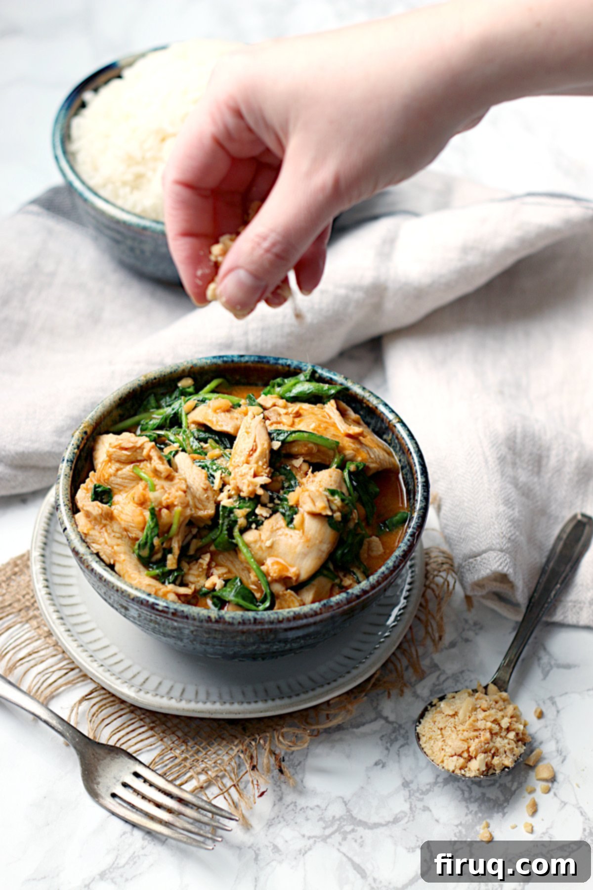 Thai Swimming Rama Chicken Garnished with Peanuts A hand sprinkling chopped peanuts into a bowl of Thai Swimming Rama Chicken.