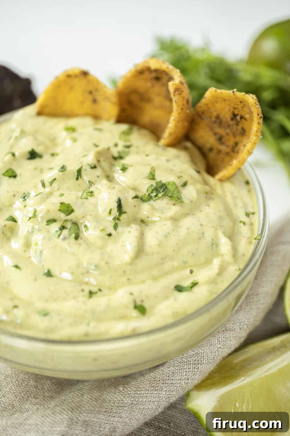 Vibrant Avocado Lime Sauce 2 avocado lime crema in a glass bowl with limes and cilantro on side and chips in the crema.