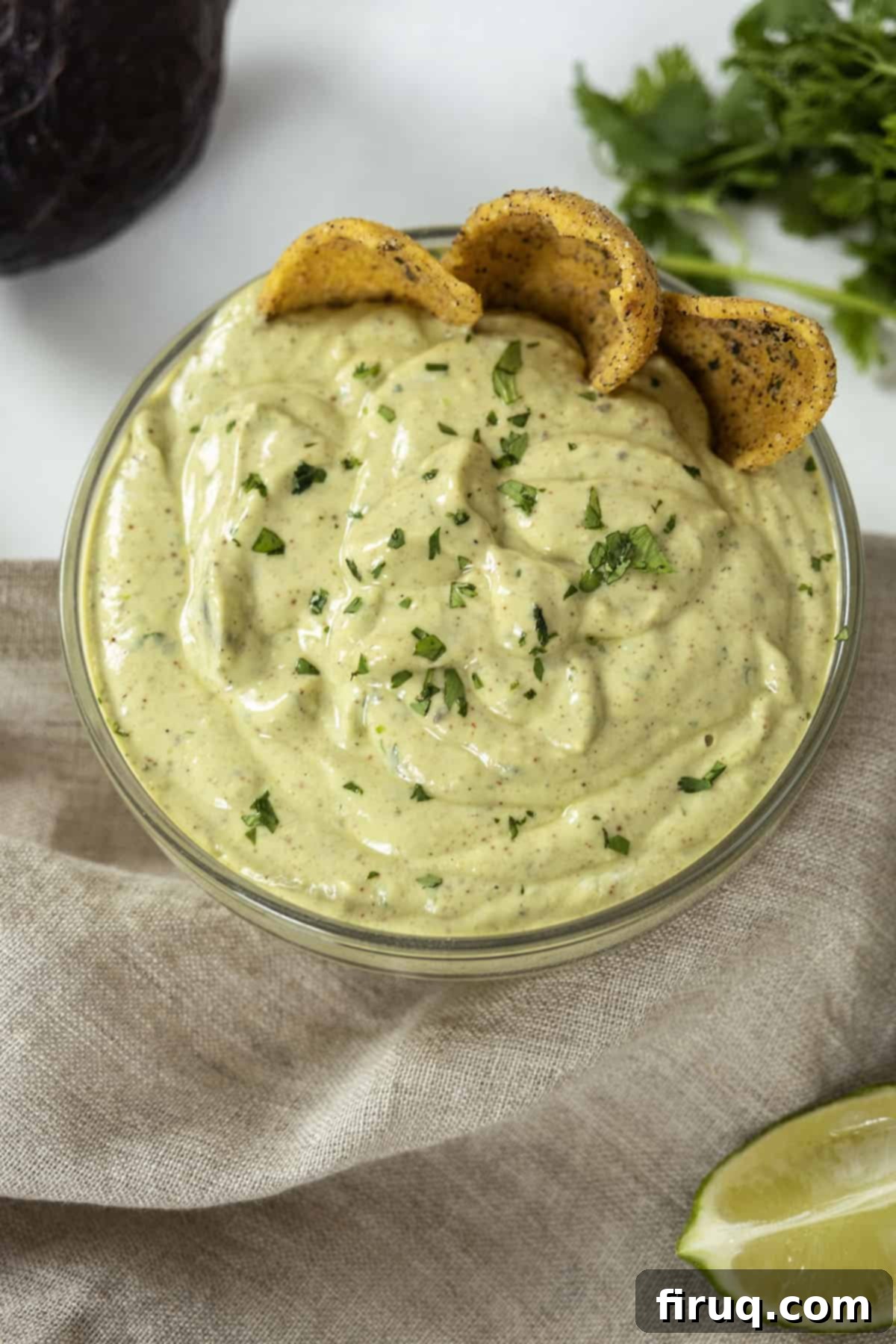 Vibrant Avocado Lime Sauce 10 avocado lime crema in a glass bowl with limes and cilantro on side and chips in the crema.