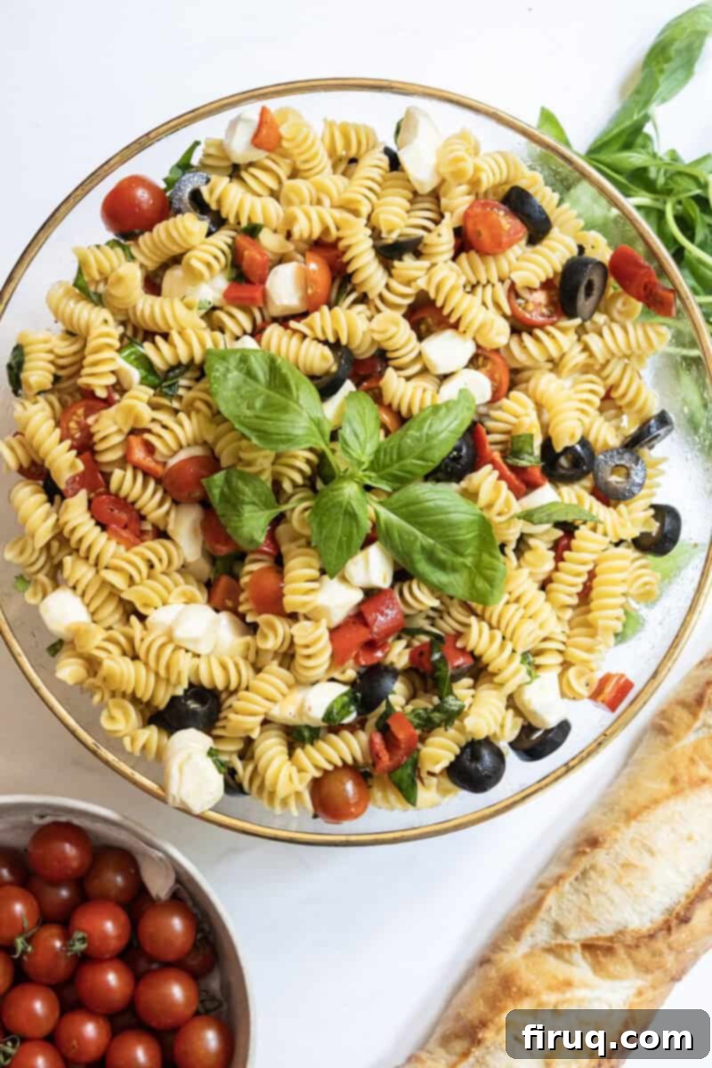 Zesty Italian Pasta Salad 2 Italian pasta salad in a large bowl with garnish of basil, on the side is a loaf of bread and bowl of cherry tomatoes.