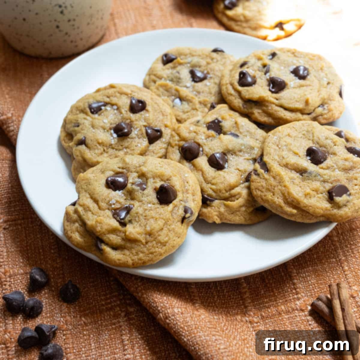 Soft and Chewy Pumpkin Spice Chocolate Chip Cookies 11 A rustic ceramic plate filled with freshly baked chewy pumpkin chocolate chip cookies, garnished with flaky sea salt.