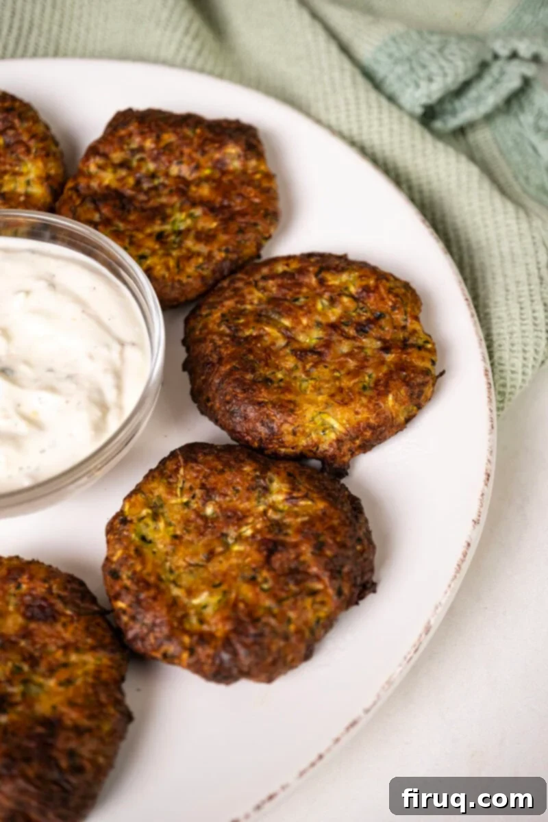 Guilt-Free Air Fryer Zucchini Fritters 2 A plate of golden-brown zucchini fritters with a side of creamy dip, garnished with fresh herbs.