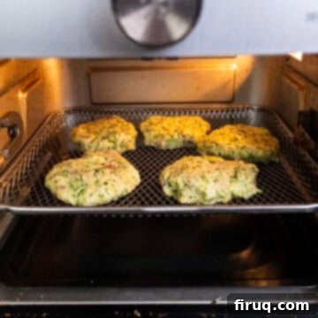 Guilt-Free Air Fryer Zucchini Fritters 10 Zucchini fritters cooking in an air fryer basket, achieving a golden-brown crisp.