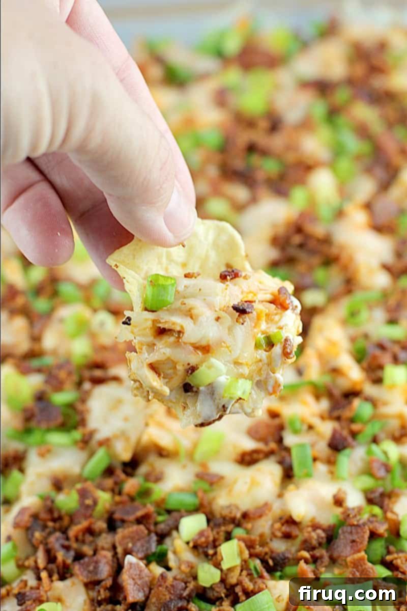 Loaded Buffalo Bacon Chicken Dip 2 Hand holding a tortilla chip scooping up creamy buffalo bacon chicken dip, highlighting the rich texture and delicious layers of chicken, cheese, and vibrant buffalo sauce.