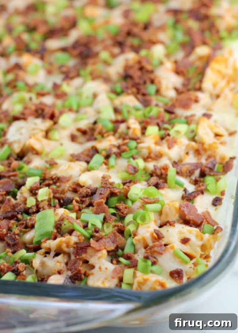 Loaded Buffalo Bacon Chicken Dip 3 Top-down view of the baked buffalo bacon chicken dip in a clear glass baking dish, showing the melted cheese and crispy bacon topping, with visible layers of creamy ranch and buffalo chicken beneath.