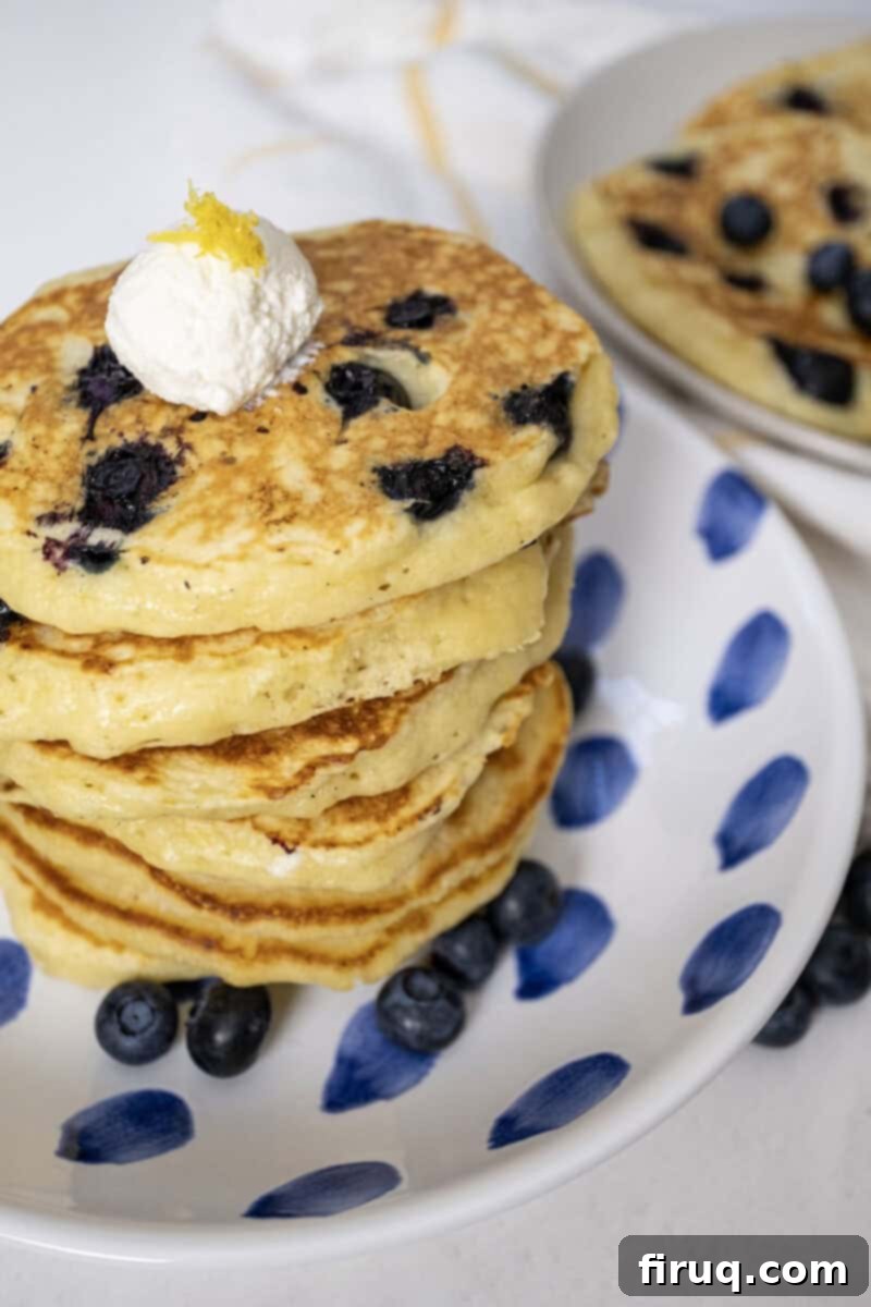 Bright Lemon Ricotta Blueberry Pancakes 2 Lemon ricotta blueberry pancakes on a plate with a dollop of ricotta.