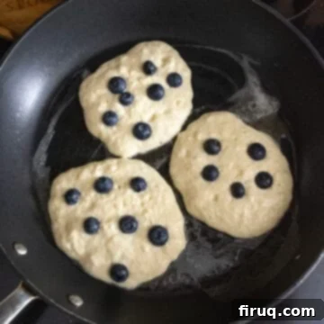 Bright Lemon Ricotta Blueberry Pancakes 9 Pancakes with blueberries baking on the frying pan.