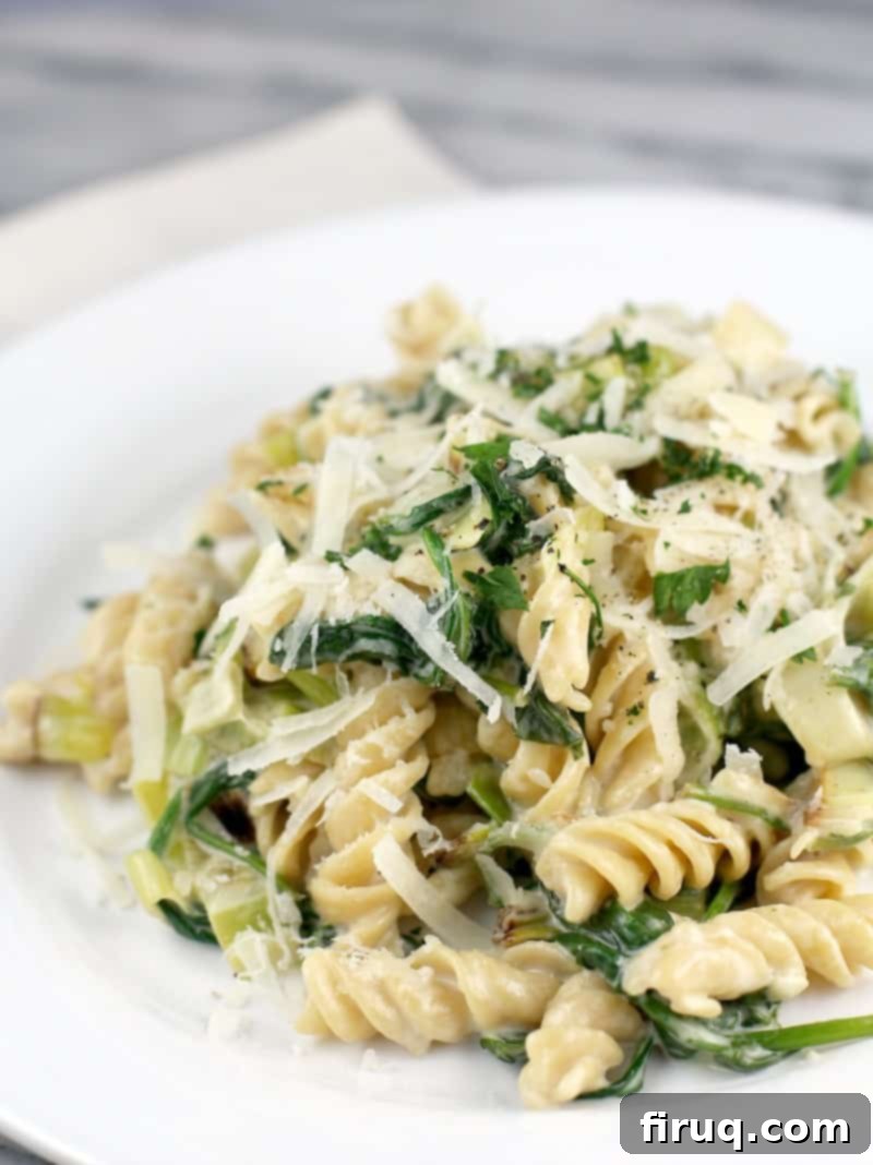 Gluten-Free Velvet Spinach & Leek Rotini 2 rotini pasta with leeks and spinach on a white plate, topped with cheese