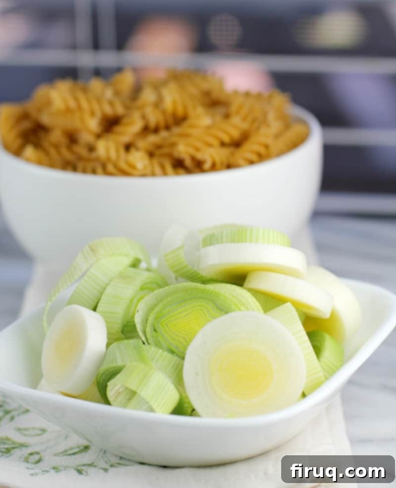 Gluten-Free Velvet Spinach & Leek Rotini 5 sliced leeks in a small white bowl; uncooked pasta in the background