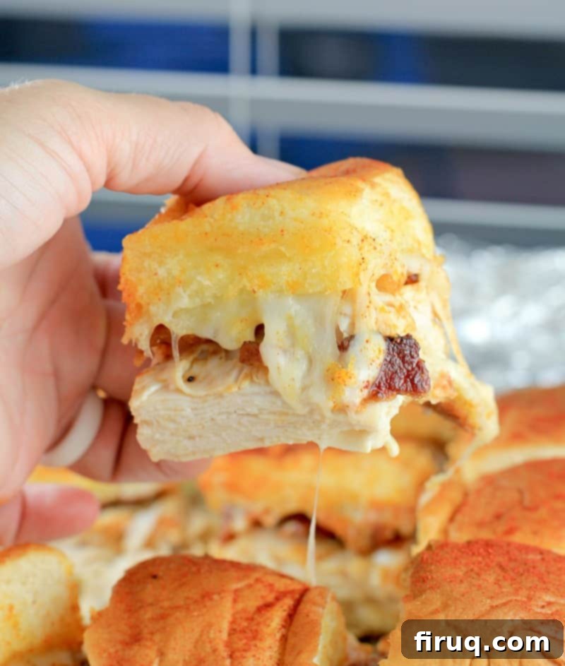 Aloha Maple Bacon Turkey Sliders 11 A close-up side view of a baked Hawaiian roll turkey slider being gently lifted, revealing the enticing layers of melted Swiss cheese, turkey, and maple bacon.