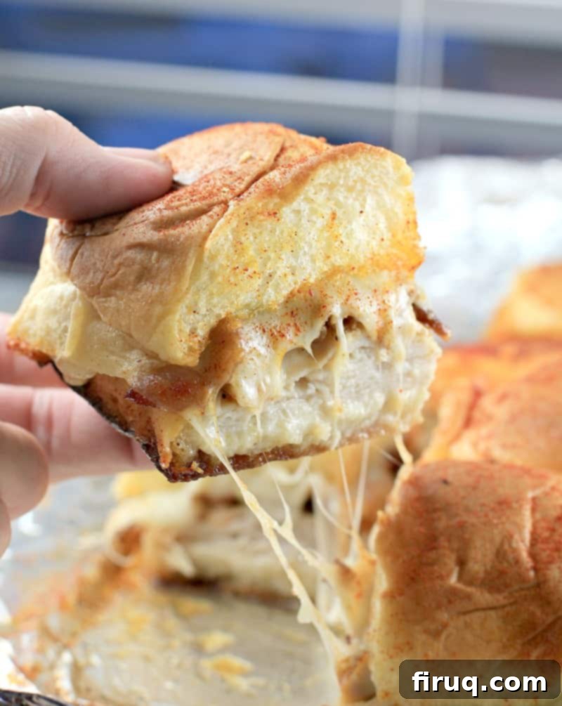 Aloha Maple Bacon Turkey Sliders 3 Side view of a single Hawaiian roll turkey slider being lifted, revealing strings of gooey, melted Swiss cheese and the savory fillings within.