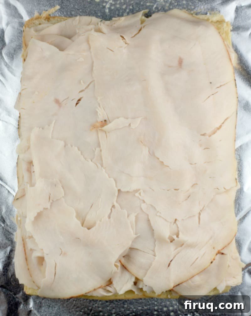 Aloha Maple Bacon Turkey Sliders 5 Top view of thinly sliced deli turkey breast generously layered over the mayonnaise-coated Hawaiian rolls, creating the base for the slider filling.