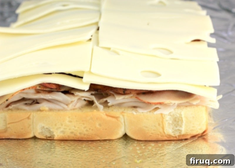 Aloha Maple Bacon Turkey Sliders 7 Side view of turkey, bacon, and Swiss cheese expertly stacked on the bottom half of a Hawaiian roll, showcasing the generous layers of filling.