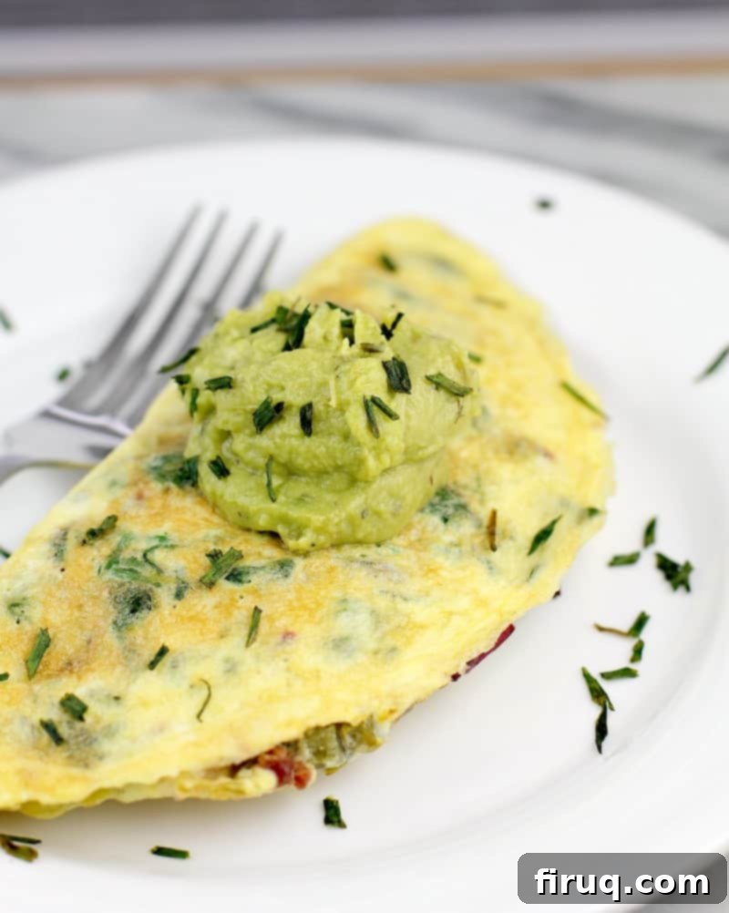 Keto Dairy-Free Bacon Jalapeno Popper Omelet 2 Omelet on white plate, topped with dollop of guacamole, snipped chives sprinkled over. Fork in the background.
