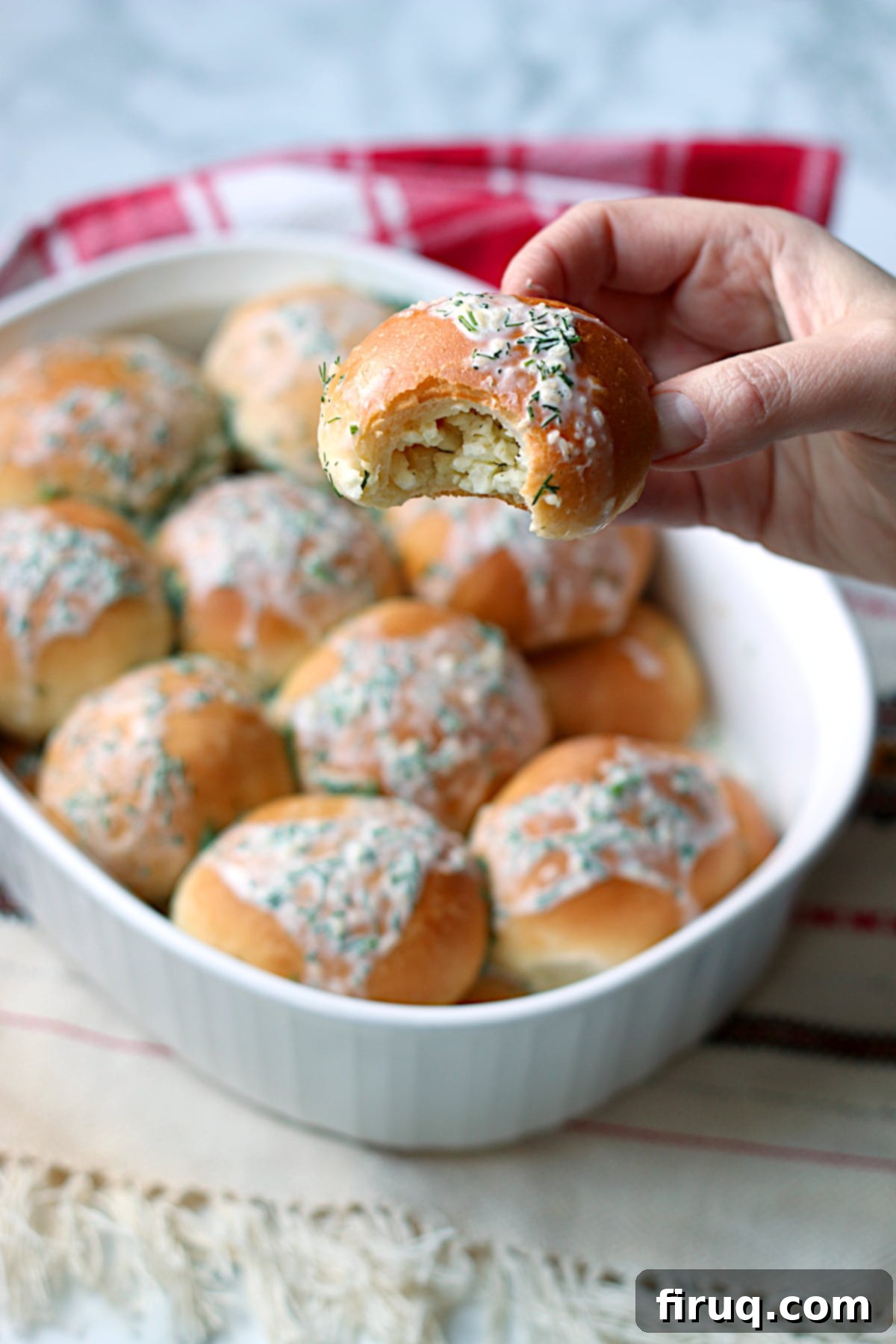 Perishky bun with savory filling A hand holding a piece of Ukrainian Perishky with a bite missing, showing the cottage cheese and dill filling.