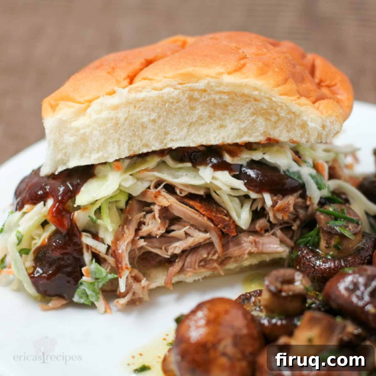 Sweet & Smoky Cola Pulled Pork 2 a pulled pork sandwich with cole slaw and bbq sauce on white plate with mushrooms.