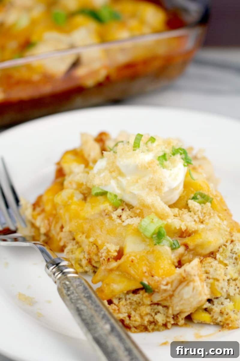 Unwrapped Keto Chicken Tamale Casserole 3 Top down view of finished casserole plated on a white plate with a silver fork, topped with sour cream and pork rind crumbs