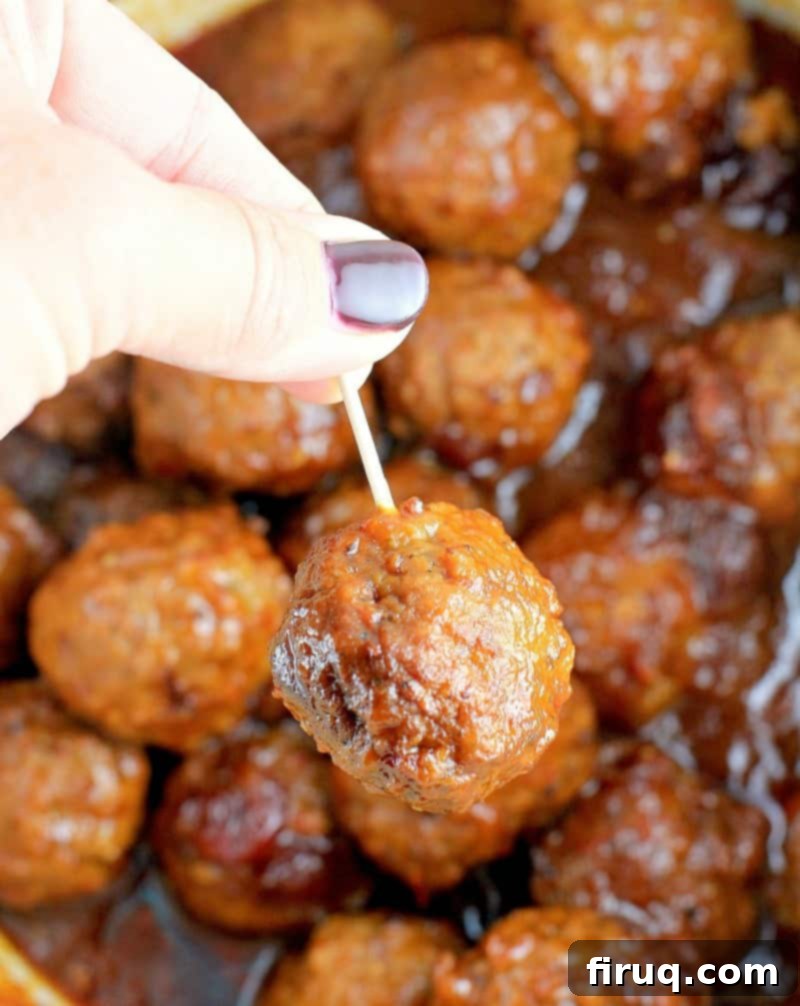 Slow Cooker Sweet Tangy Cranberry BBQ Meatballs 2 hand lifting a meatball out of the crockpot on a toothpick