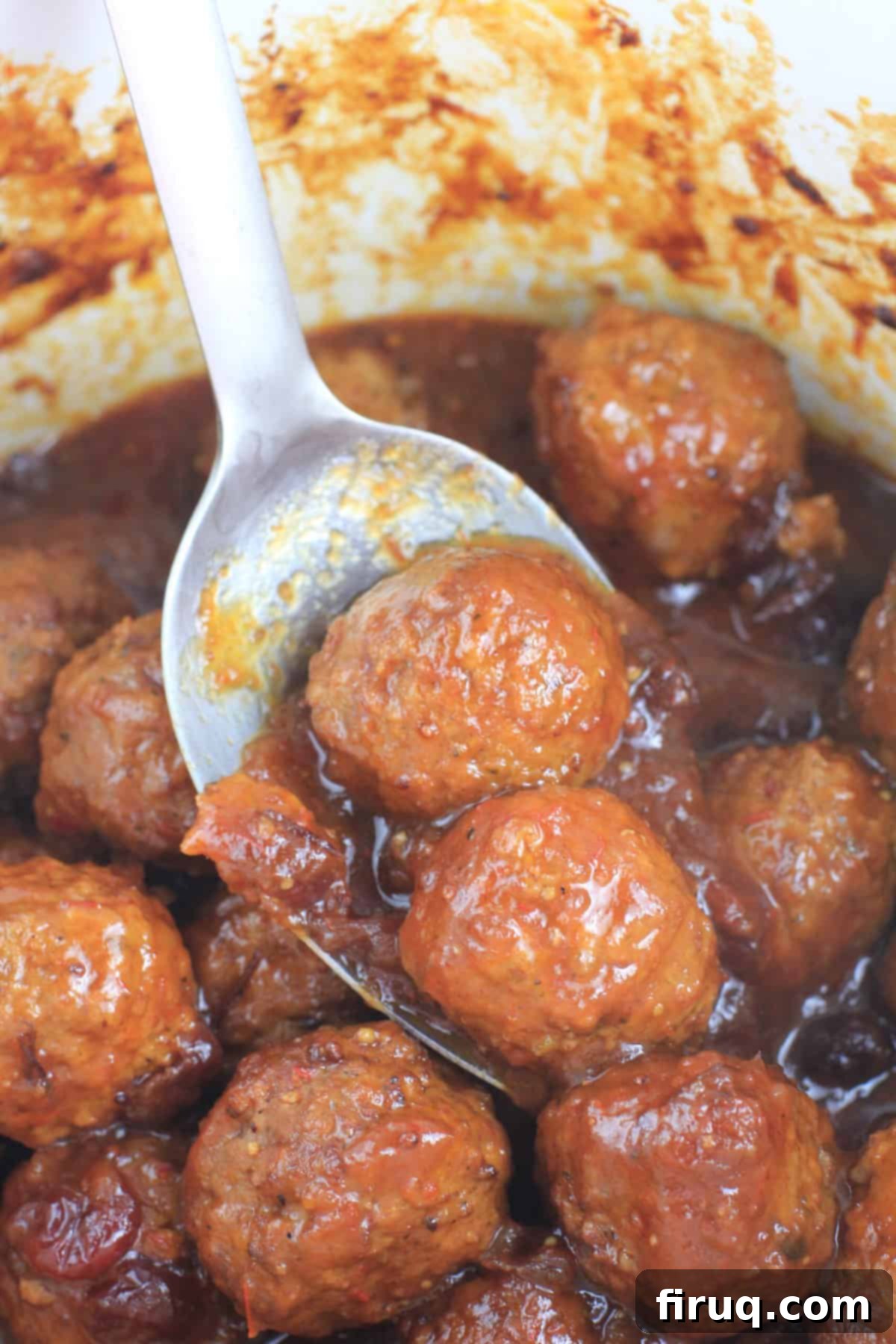 Slow Cooker Sweet Tangy Cranberry BBQ Meatballs 7 large metal spoon with 2 meatballs out of the crockpot