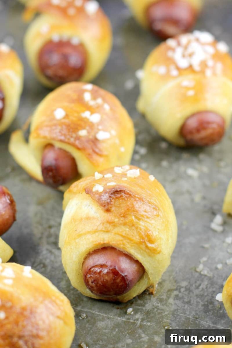 Golden Pretzel Piggy Bites with Tart Red Currant Dip 2 angled view of cooked mini pretzel pigs on a grey bake sheet sprinkled with salt