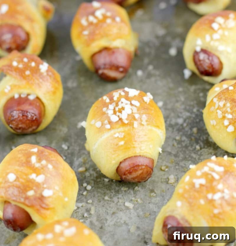 Golden Pretzel Piggy Bites with Tart Red Currant Dip 3 zoomed out view of cooked mini pigs in a blanket on a bake sheet sprinkled with salt