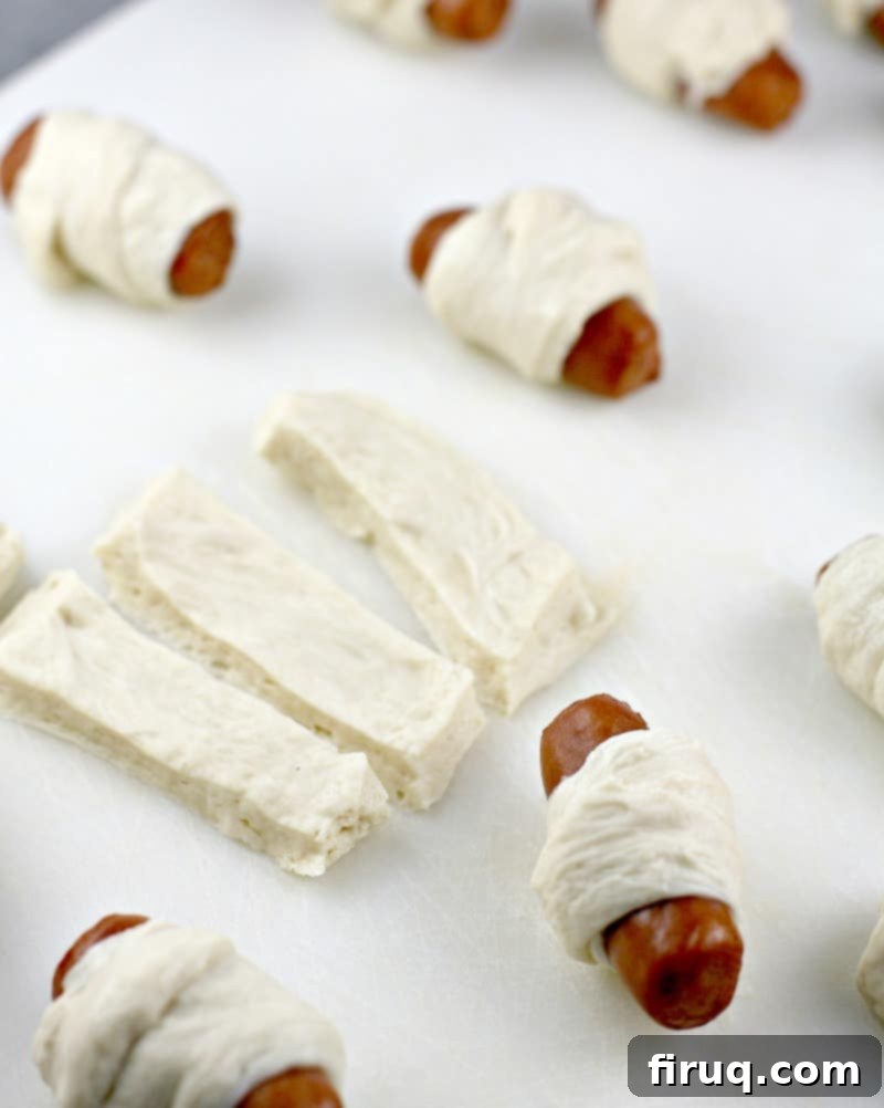 Golden Pretzel Piggy Bites with Tart Red Currant Dip 4 strips of pizza dough with several wrapped mini pigs in blankets on a white board