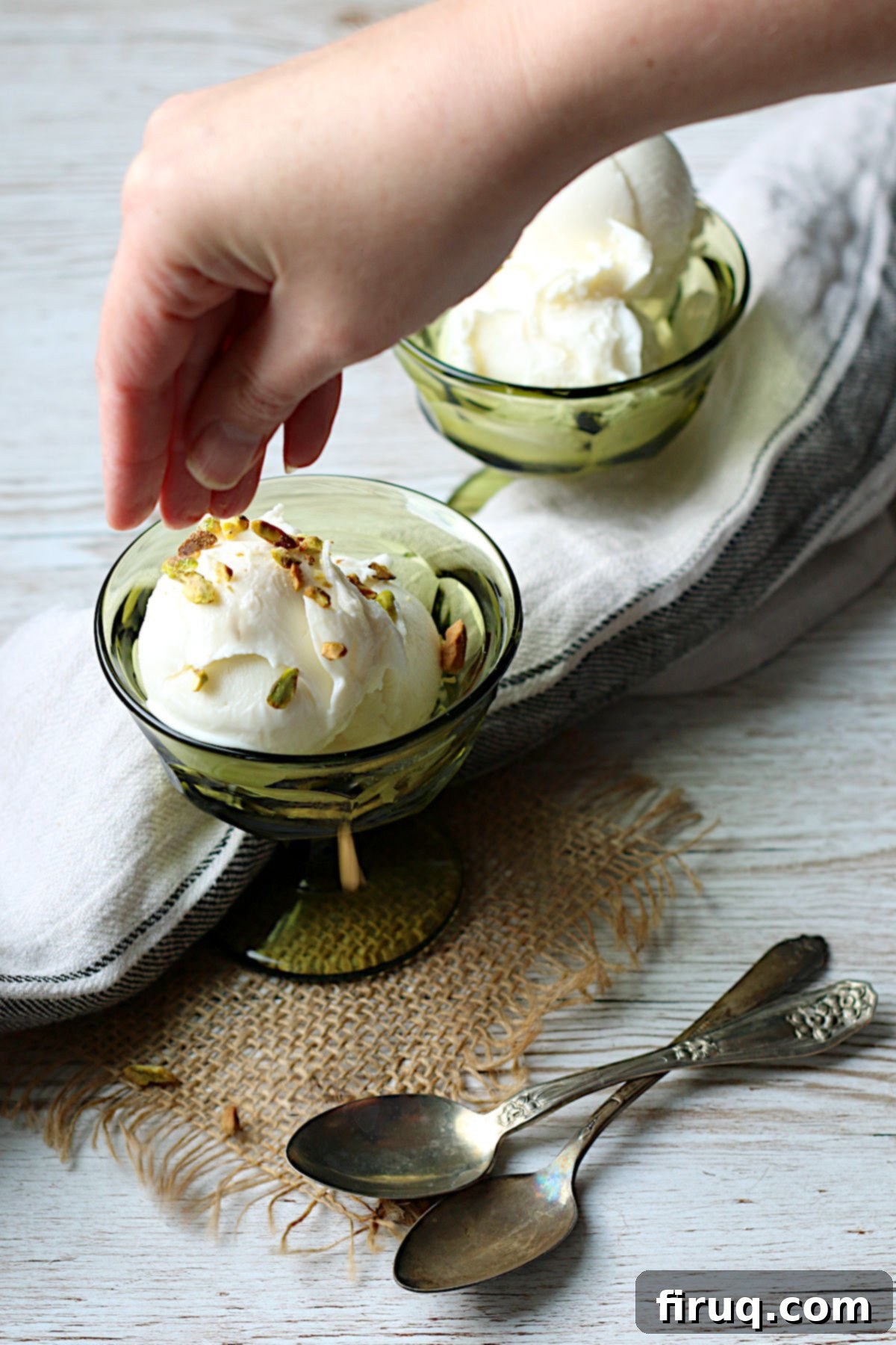 Booza-Inspired Ice Cream with Pistachios A hand sprinkling chopped pistachios on a small dish of Booza-Inspired Ice Cream, highlighting the garnish and appealing texture.